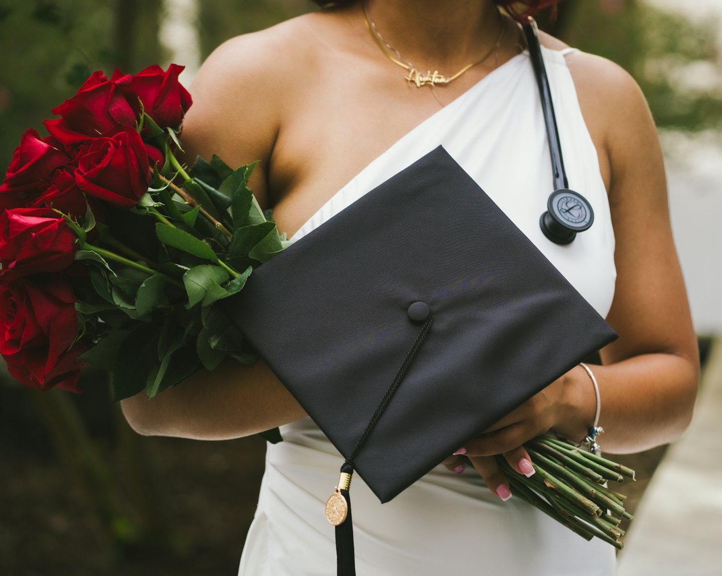 Graduate in a white gown holding red roses and a stethoscope.