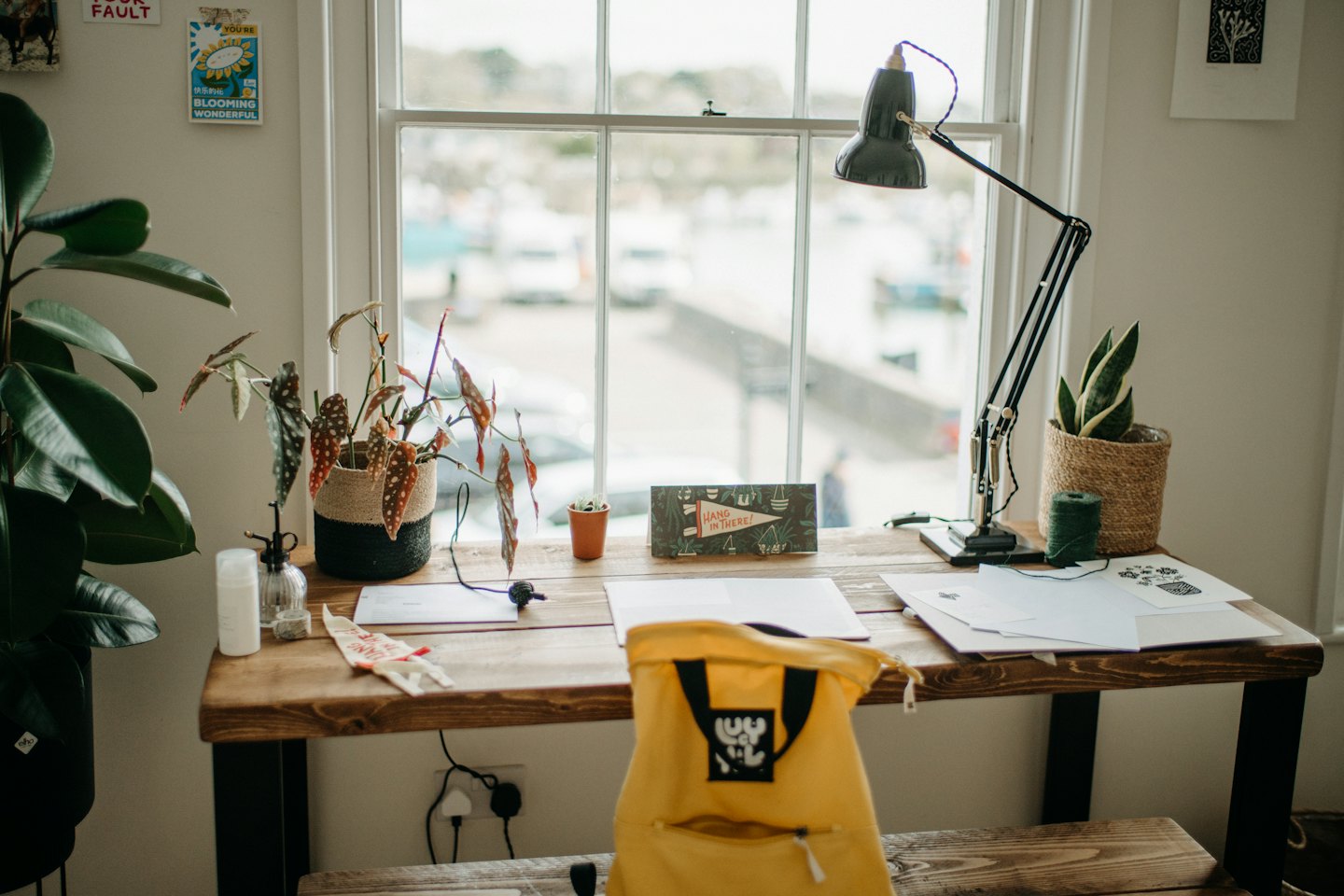 Rustic wooden desk with plants and yellow backpack in a bright home office.